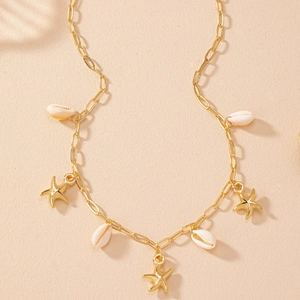 Flat lay of gold starfish pendants and white cowrie shells on a sandy texture backdrop