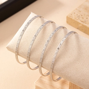 Set of four silver diamond-patterned metal bangles displayed on a cream jewelry roll