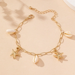 Flat lay of gold starfish and seashell bracelet on a warm sandy beach background