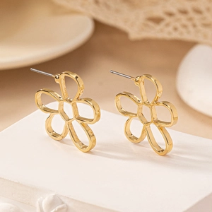 Detail view of hollow gold floral earrings with elegant metal outlines on a display stand