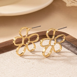 Minimalist golden hollow flower earrings with elegant lines on beige woven cushion
