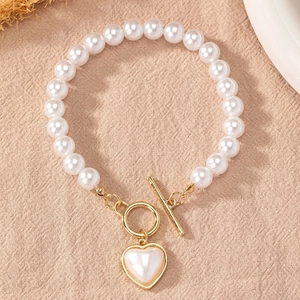 Détail d'un bracelet de perles avec pendentif cœur et fermoir OT doré sur tissu