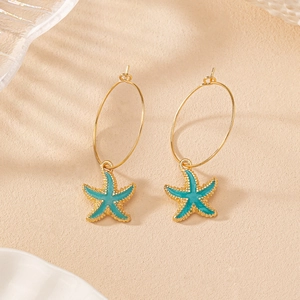 Détail de boucles d'oreilles étoile de mer dorées avec émail bleu et texture