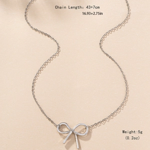 Minimalist silver bow pendant necklace with adjustable chain on warm textured background
