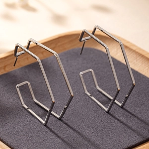 Polished silver geometric hexagonal hoop earrings displayed on a minimalist wooden tray