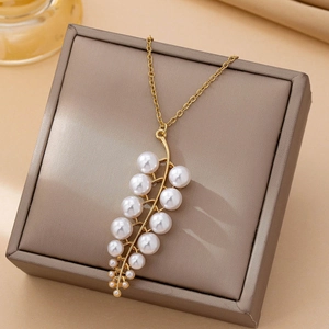Elegant gold leaf branch necklace with white pearls displayed on a brown leather box