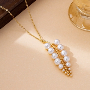 Detailed view of a gold leaf pendant necklace with eleven white pearls on a textured background