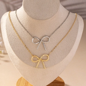 Minimalist bow tie necklaces in gold and silver finish displayed on a beige jewelry bust