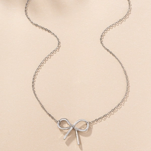 Flat lay macro of minimalist silver bow pendant necklace on a beige textured background