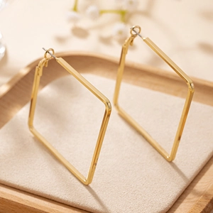 Detail view of large geometric square earrings in shiny gold on a soft beige display