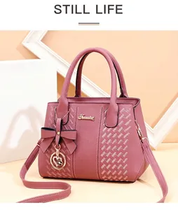 Détail du sac à main rose poudré avec texture tissée et breloque coeur sur support épuré