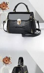Detail view of glossy black crocodile embossed handbag with golden metallic lock buckle
