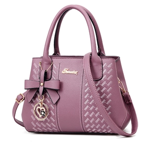 Sac à main violet élégant en cuir grainé avec nœud et pendentif cœur sur fond blanc