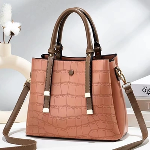 Detail of pink faux crocodile leather bag with brown handles and golden hardware