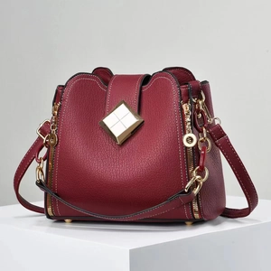 Sac seau bordeaux en cuir grainé avec boucle dorée élégante posé sur un socle blanc