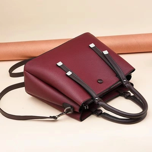 Detail of burgundy lychee leather handbag featuring dark brown straps and silver buckles