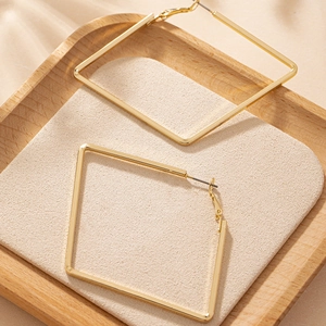 Macro shot of large golden geometric square hoop earrings with polished finish on wooden tray