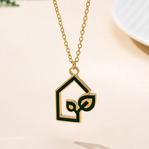 Detailed view of the gold house-shaped pendant with green enamel leaf inlay and fine chain