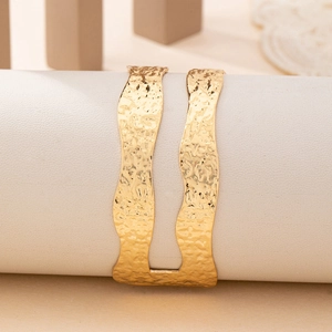 Chic hammered gold cuff bracelet with irregular wavy edges on white leather stand