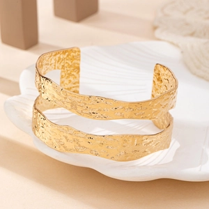 Detail of two gold hammered open bracelets on a white shell plate with minimalist decor