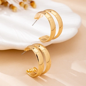 Elegant gold double C-shaped hoop earrings displayed on a white shell tray with dried flowers