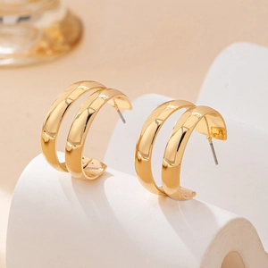 Detailed view of dual-loop gold C-shaped earrings with a polished mirror finish on white stand