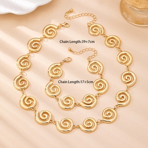 Ensemble collier et bracelet dorés avec motif tourbillon évidé sur fond beige chaud