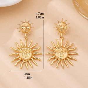 Vintage golden sun earrings with relief face design on a textured beige surface