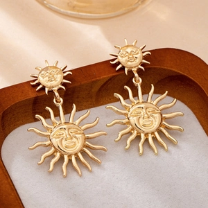 Elegant gold sun drop earrings with human face design and wavy rays on wooden tray