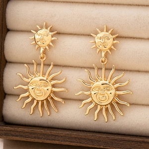 Macro detail of gold sun earrings with double-layered face reliefs on beige velvet tray