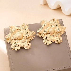 Macro detail of golden floral earrings with radial pleated petals on dark gift box