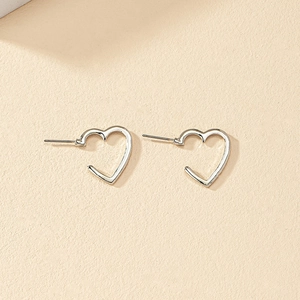 Detailed close-up of hollow silver heart stud earrings on a clean beige surface