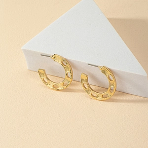 Close-up of golden C-shaped textured earrings with cutout design on a geometric display