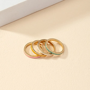 Detail view of four minimalist gold-tone stackable rings with colorful enamel stripes