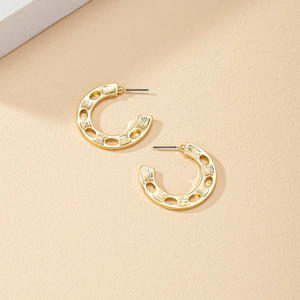 Textured gold C-shaped hoop earrings with hollow cut-outs on beige background