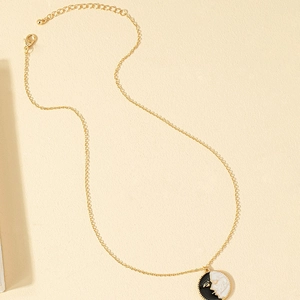 Vintage gold coin necklace with black and white moon face pendant on beige background