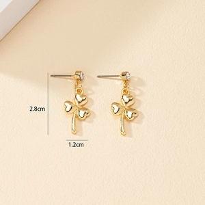 Boucles d'oreilles trèfle doré avec pétales en cœur et strass sur fond beige