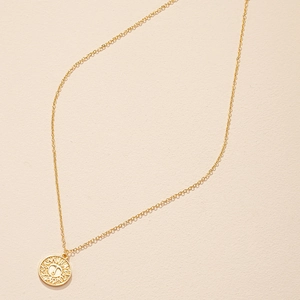 Golden sunburst coin necklace featuring Aries zodiac symbol on minimal cream backdrop