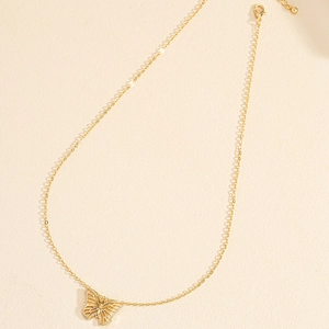 Collana dorata con pendente a farfalla traforata su uno sfondo beige con texture fine