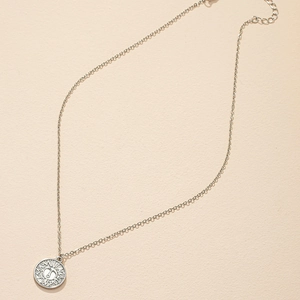 Detailed view of silver coin pendant with sun pattern and fine metal chain on beige texture
