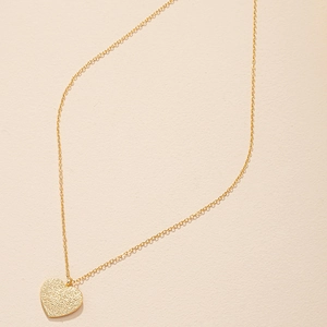 Golden matte heart pendant necklace with delicate O-chain on textured beige background