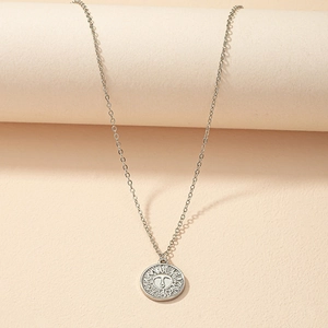 Macro detail of silver sun face coin pendant on a minimalist thin chain necklace