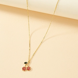 Collier chic en chaîne dorée avec pendentif cerise en émail rouge sur fond beige texturé