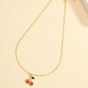 Collier chic en chaîne dorée avec pendentif cerise émaillé rouge sur fond beige texturé