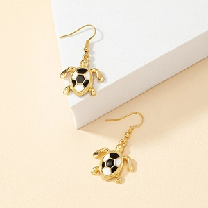 Gold-plated turtle drop earrings with black and white enamel shells on a minimalist stone