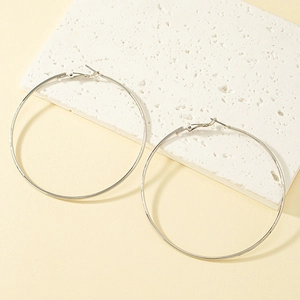 Minimalist large silver circle hoop earrings displayed on a white textured stone base