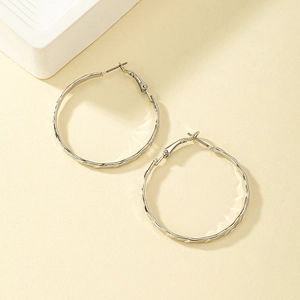 Boucles d'oreilles créoles argentées texturées au design ondulé sur fond beige