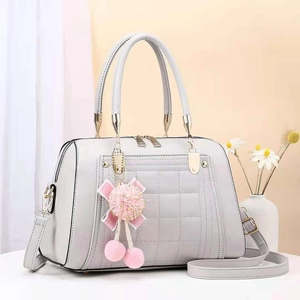 Close-up of light grey quilted tote bag with golden hardware and pink pompom charm