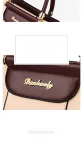 Detail of burgundy and beige leather handbag featuring a gold Danbaoly metal logo plaque