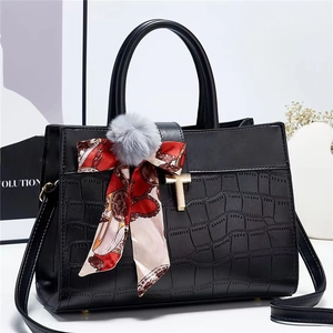 Detail of black crocodile texture handbag with gold T-lock and floral scarf charm